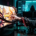 A hooded person reaching for a Download Now button as black tentacles with binary code emerge from the screen