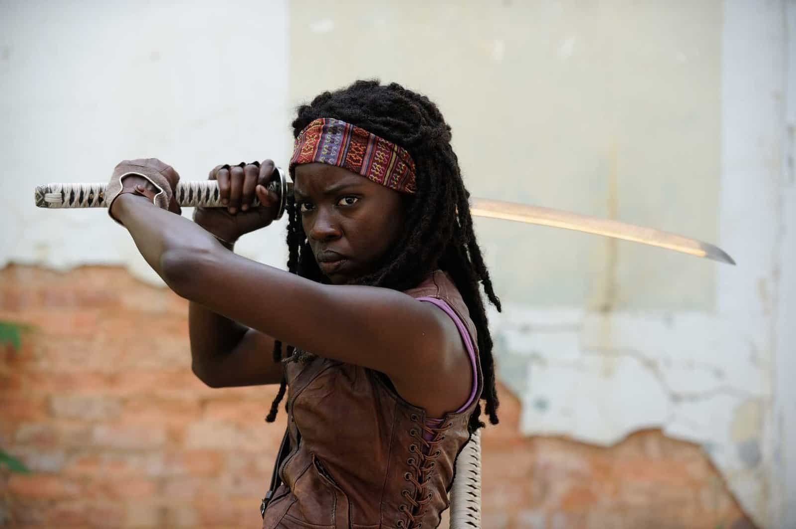 Michonne (Danai Gurira), a Black woman with dreadlocks held back by a colorful bandana, stands in a ready stance with a katana in The Walking Dead