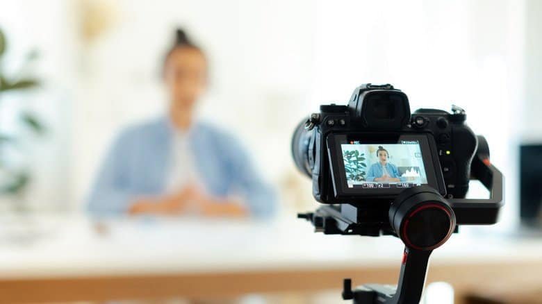 A blurred view of a person, with a digital camera prominently recording them