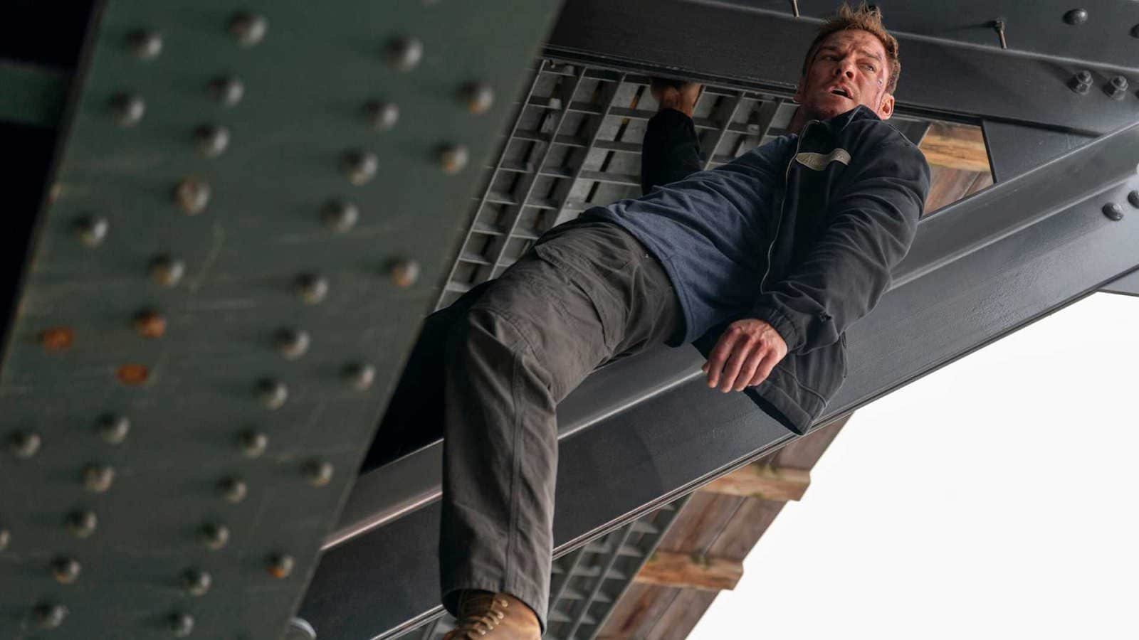 Alan Ritchson as Reacher hanging from a bridge in season 4